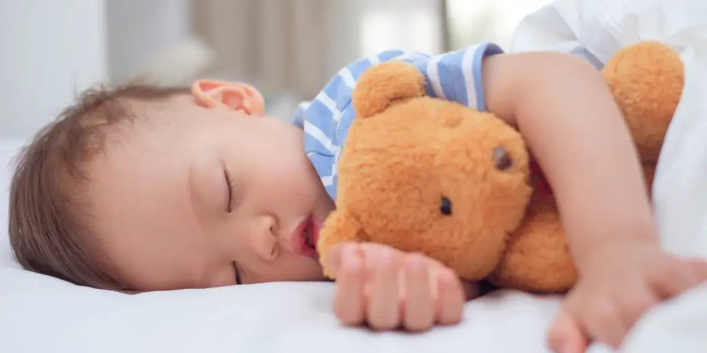 Bébé garçon qui dort sur le côté avec son ours en peluche dans les bras