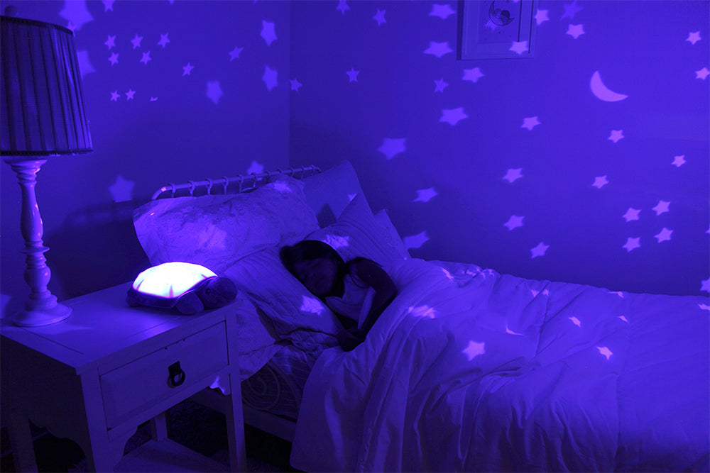 Enfant qui dort dans son lit avec une veilleuse en forme de tortue à projection de ciel étoilé allumée