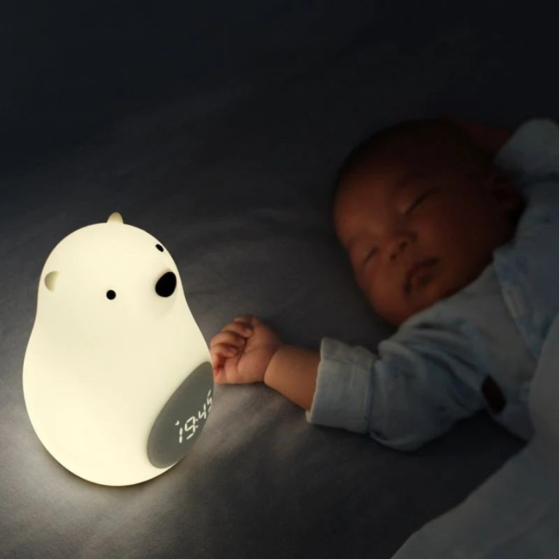 Réveil veilleuse en forme d'ours posé sur un lit à côté d'un bébé qui dort