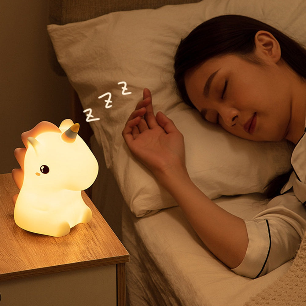 Veilleuse en forme de bébé licorne lumineuse sur une table de chevet à côté d'une femme qui dort