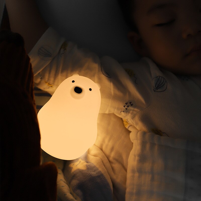 Veilleuse pour bébé en forme d'ours polaire lumineux à côté d'un bébé qui dort dans la nuit