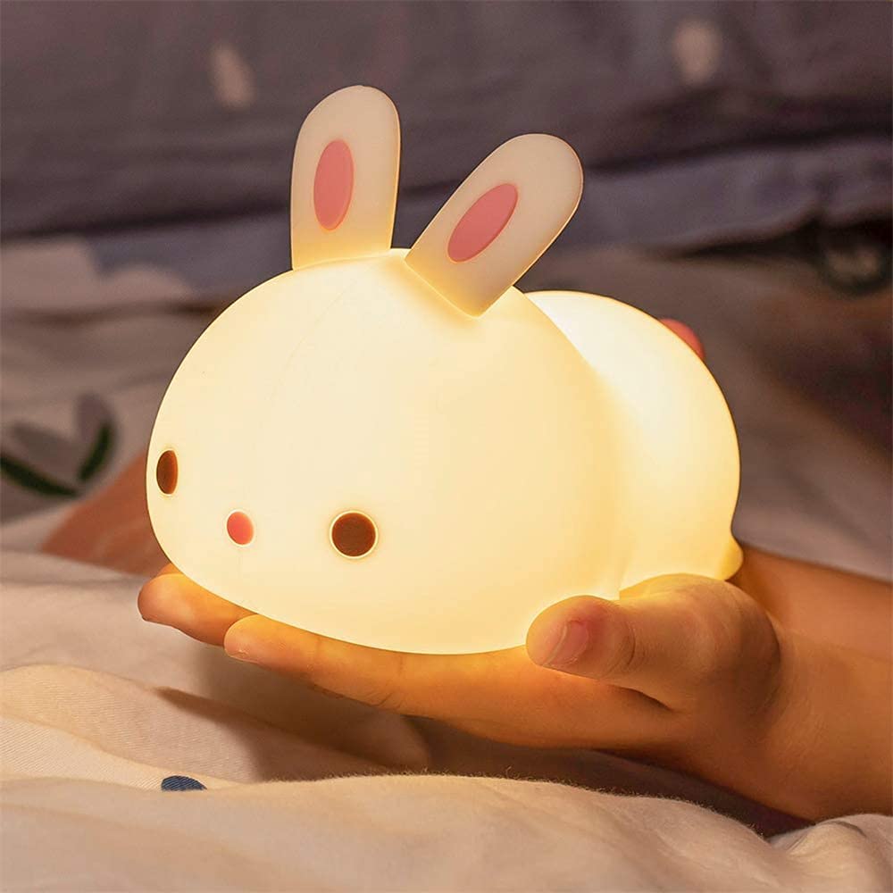Veilleuse en forme de bébé lapin présenté sur une main avec la fonction lumineuse activée
