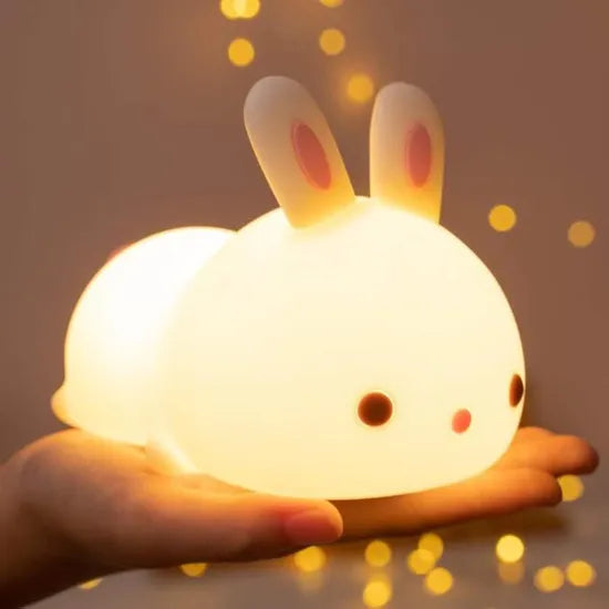 Veilleuse en forme de bébé lapin présenté sur une main avec la fonction lumineuse activée, vue de profile