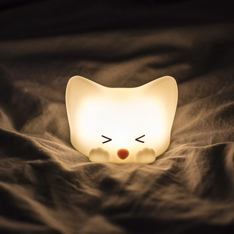 Veilleuse en forme de bébé chat lumineux posée sur un lit
